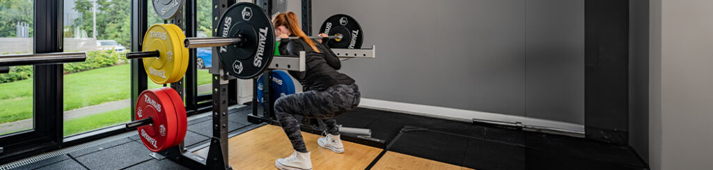 Female bodied person performing a squat on a squat rack. 
